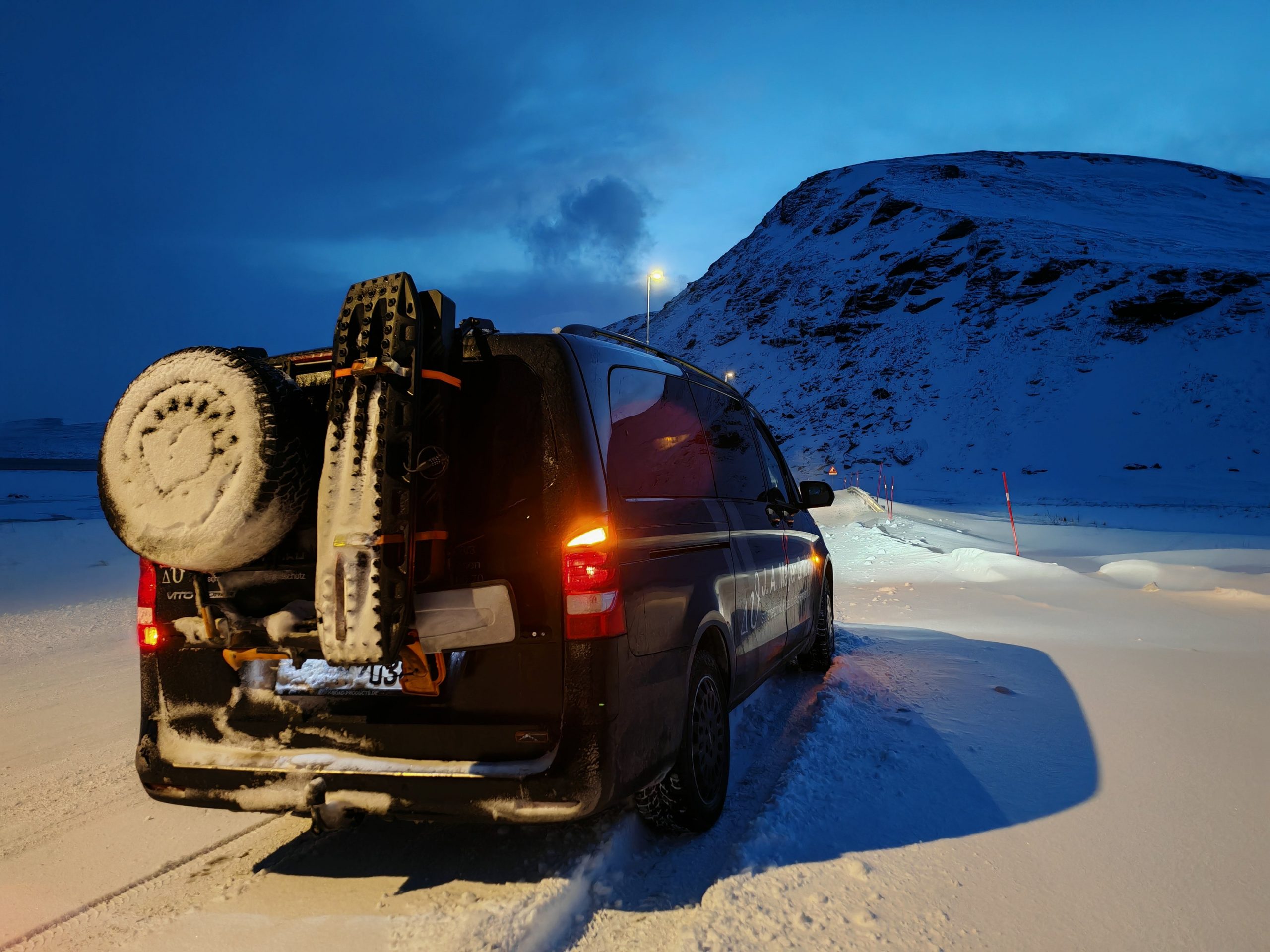 Mercedes Vito in Dämmerlicht, eingeschneites Heck, eingeschneite Schneelandschaft, Bergkulisse im Hintergrund, Stimmung einer Winterreise.